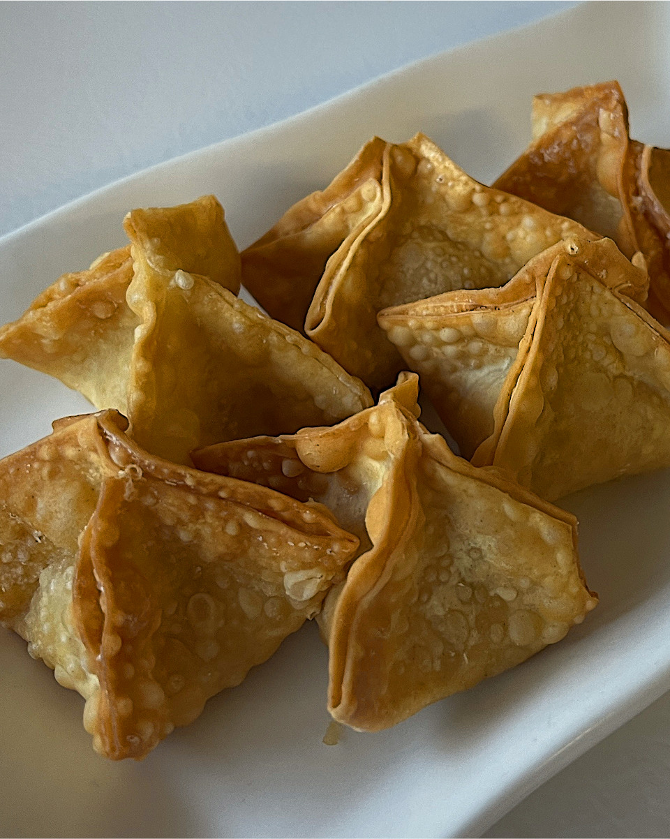 Golden-brown fried cream cheese and crab dumplings with crisp, folded wrappers on a white plate