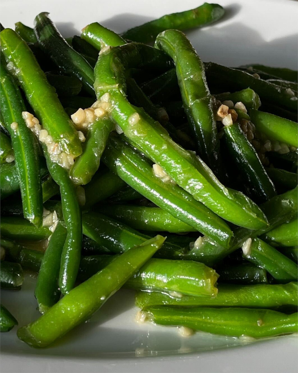 Sautéed green beans coated with chopped garlic on a white plate