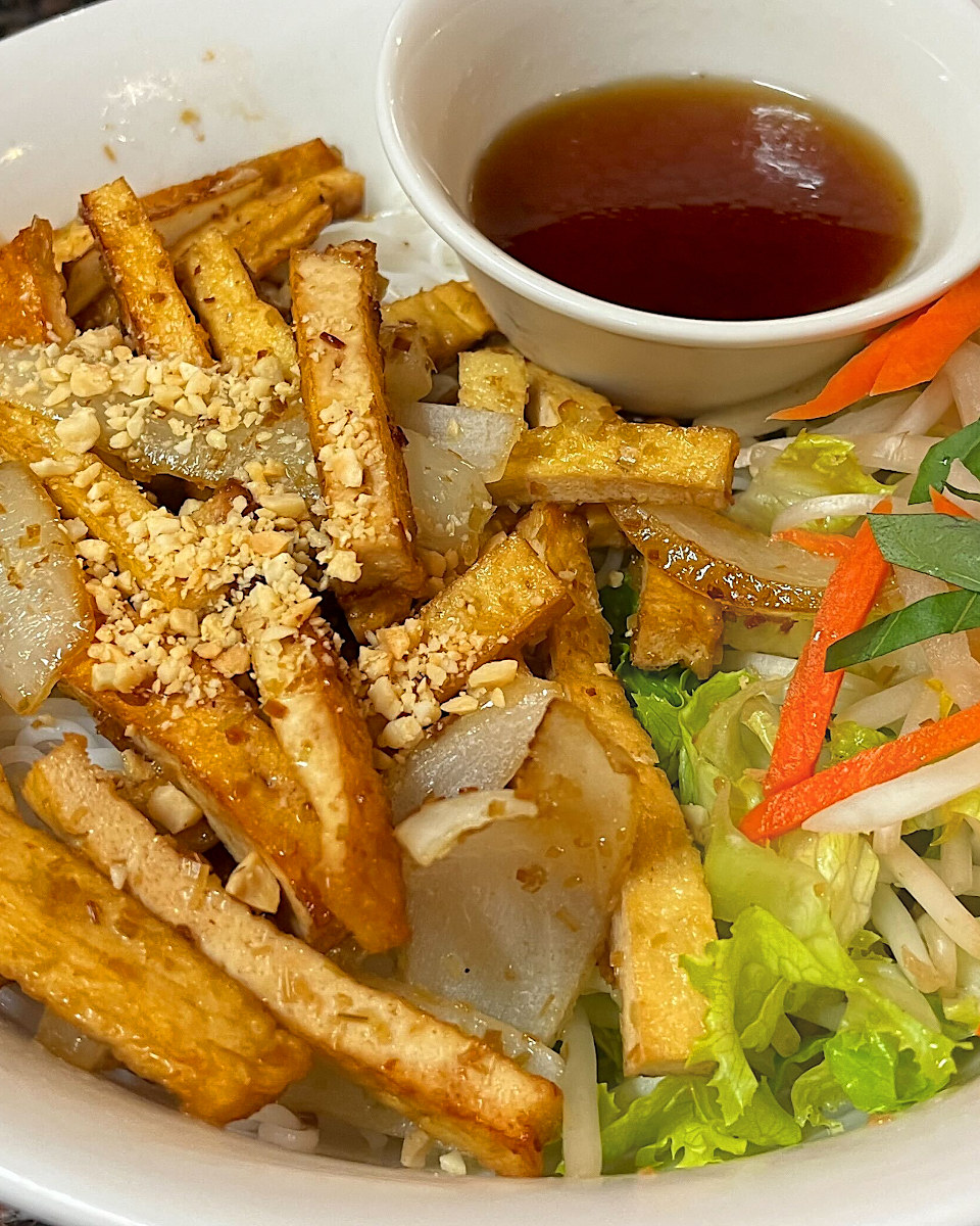 Golden lemongrass tofu and onions over vermicelli with crushed peanuts, vegetables, and dipping sauce