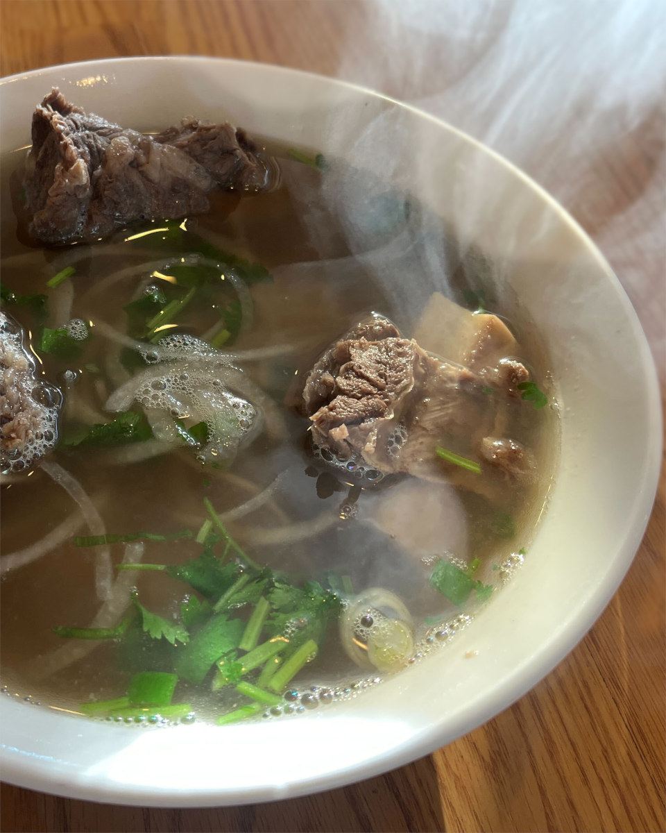 Steam rising from short rib pho with beef ribs, sliced onions, and cilantro in broth