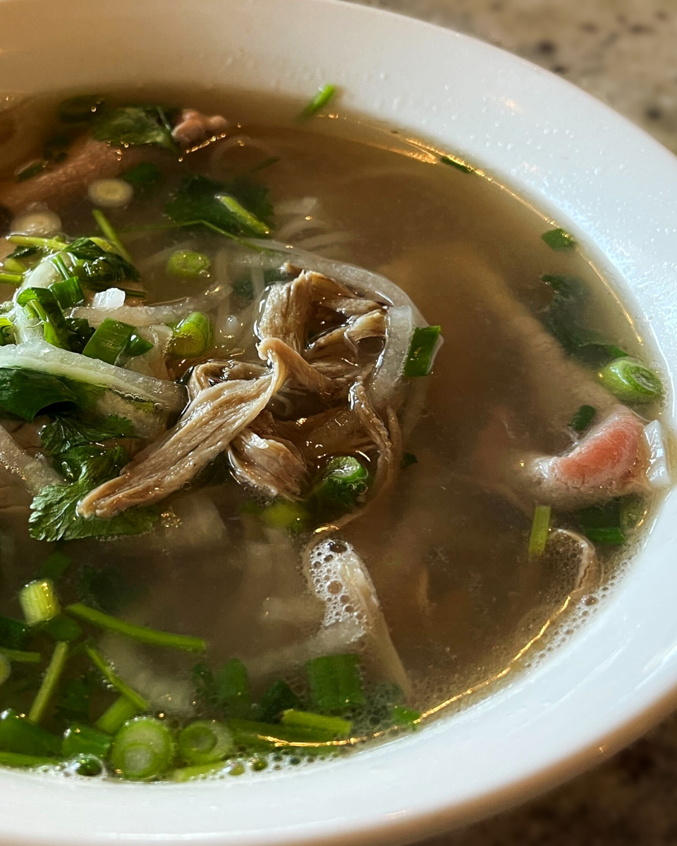 Rice noodle soup with beef bone broth topped with sliced brisket and eye of round steak in it. Green onion, white onion, and cilantro add fresh green color.